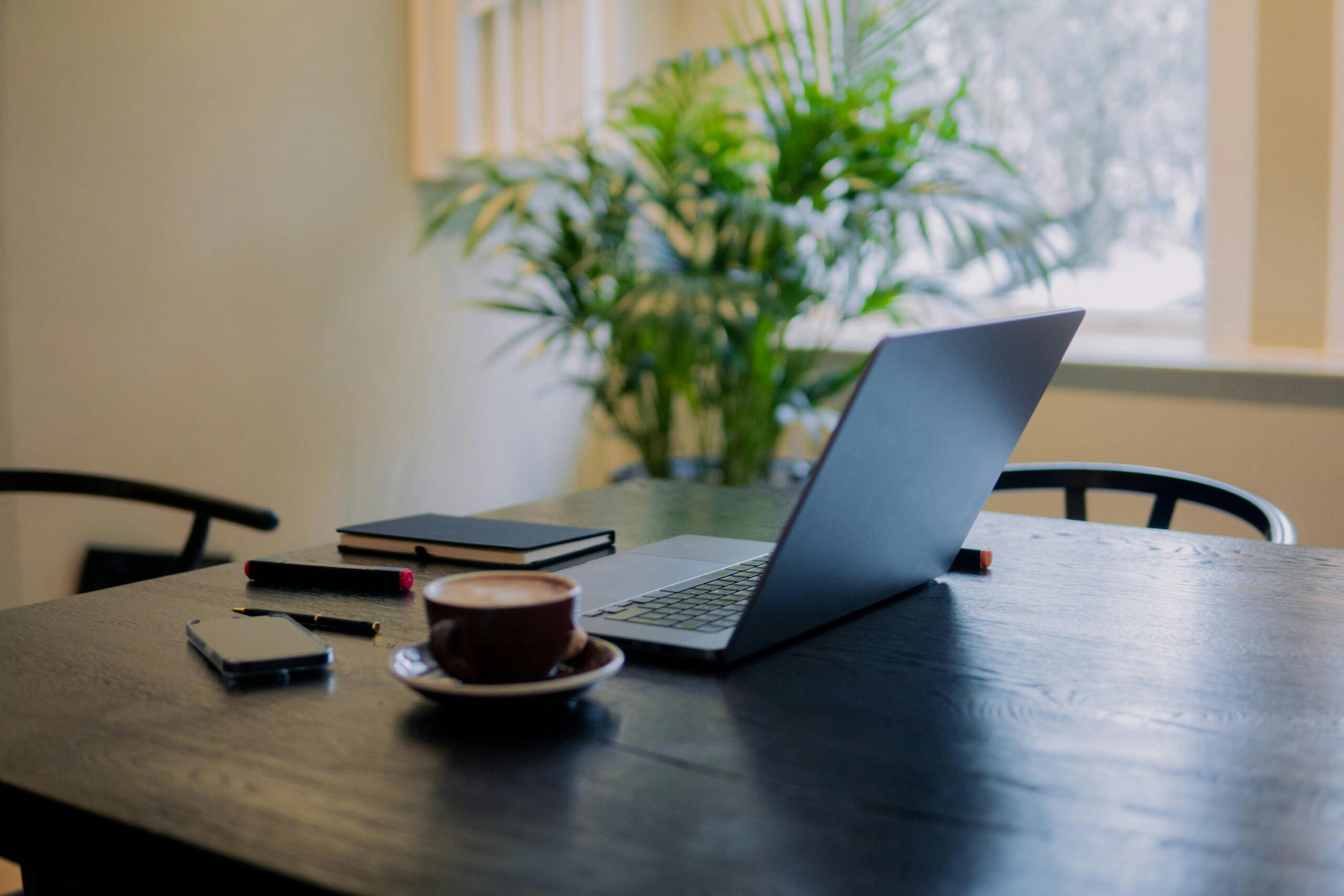 Home A warm, inviting workspace in Amsterdam featuring a laptop, coffee, and potted plant.